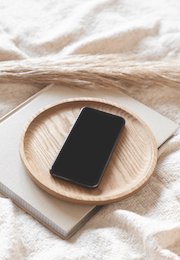 Cell phone in a wooden tray on top a book in linen bedding
